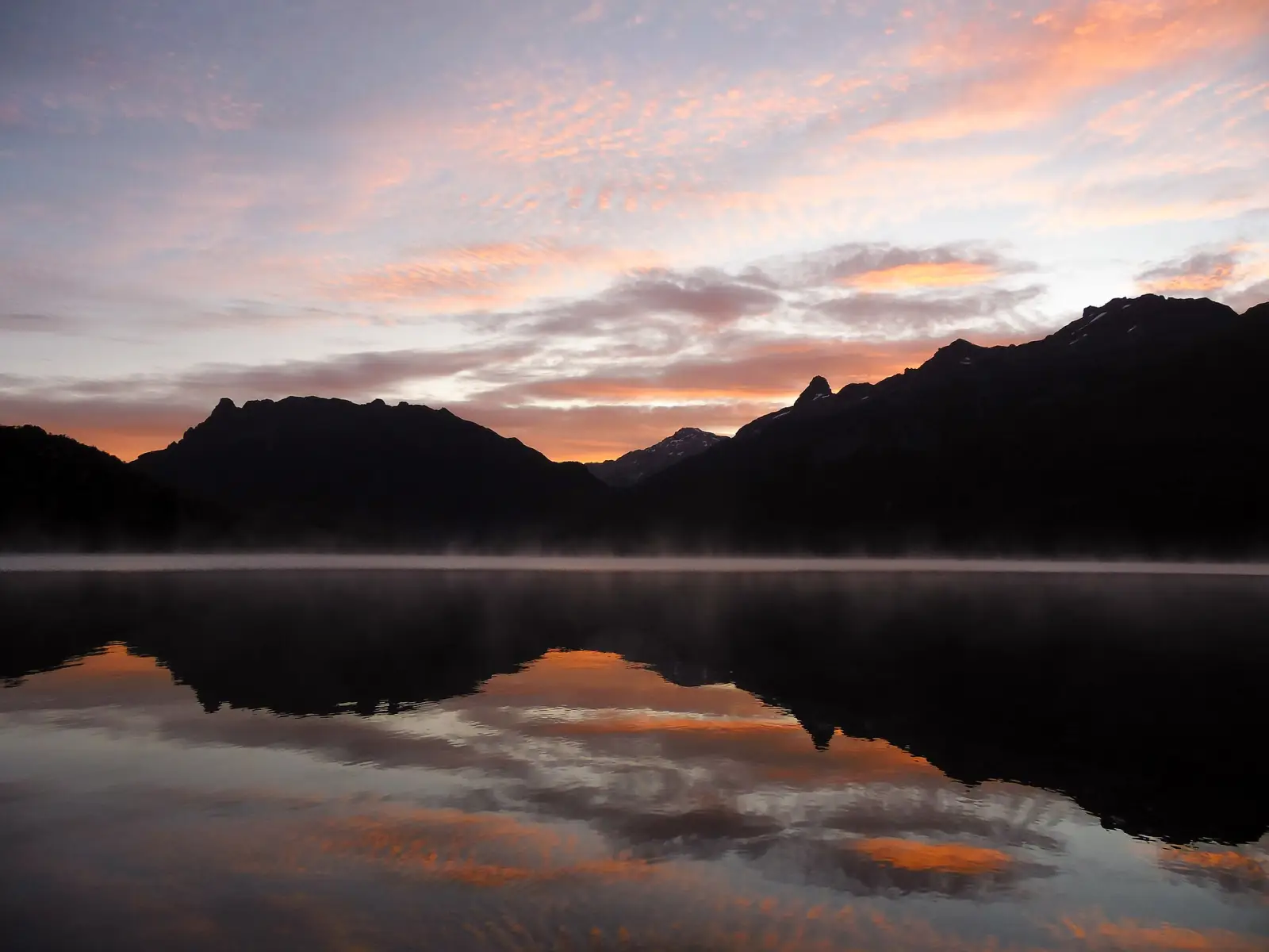 Amanecer sobre el lago General Pinto Concha en el Parque Nacional Hornopirén, con montañas reflejadas en el agua